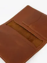 Porta pasaporte de cuero color marrón, con costuras a tono y logo grabado en la parte inferior.