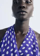 Vestido corto de poliéster, color azul con estampado de lunares blancos. Presenta cuello pico cruzado, tirantes anchos y diseño evasé con cierre lazo cruzado en la cintura.