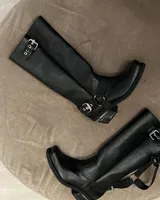 Bota alta de cuero vacuno color negro, con caña recta, punta cuadrada y estribo desmontable.