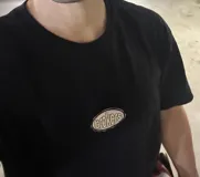 Remera negra de corte boxy con parche ovalado con texto en el frente.