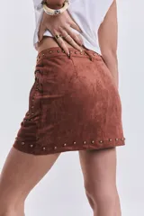Mini pollera marrón de gamuza con tachas doradas, cierre lateral con cremallera y corte ajustado.