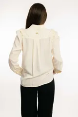 Camisa tipo seda color crema, con volados en el hombro y frunce en la manga, diseño elegante.