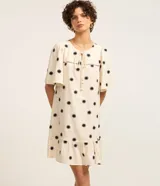 Vestido corto evasé color crema con estampado de soles negros, cuello redondo con lazo, mangas cortas y bajo con volantes.