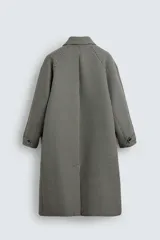 Abrigo largo de corte recto con estampado de cuadros en blanco y negro. Tiene cuello solapa, manga larga, bolsillos laterales y cierre frontal con botones.
