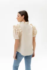 Camisa de lino color lila con volados en el cuello y en las mangas cortas abullonadas. Presenta un diseño de corte recto con cierre frontal de botones.