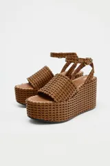 Sandalias con plataforma tipo cuña color marrón, con cuerpo trenzado, tira delantera y cierre mediante tira con hebilla a la pulsera del tobillo.