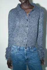 Chaqueta de punto azul con cuello solapa, manga larga y flecos en las mangas. Cierre frontal con botones.