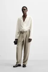 Pantalón negro de corte amplio, con pliegues frontales, bolsillos laterales y traseros de ojal. Incluye cinturón de la misma tela con hebilla metálica.