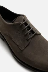 Zapato de vestir tipo derby color marrón oscuro, con capellada de cuero serraje, horma redonda, cordones finos al tono y suela con ligero tacón.
