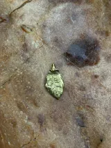 Dije de bronce con forma de hoja, modelado y tallado a mano.