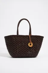 Bolso tipo tote de mimbre trenzado color marrón con doble asa corta y dije circular dorado con letras.