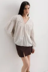 Camisa celeste de algodón con bordado calado, cuello en V y mangas largas abullonadas con puños elásticos.