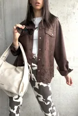 Sobrecamisa marrón de gamuza sintética, corte oversize, con cuello camisero, cierre frontal con botones a presión, mangas largas con puños abotonados, bolsillos de parche en el pecho y detalle de calado con motivos florales en el ruedo.