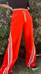 Pantalón de jogging color gris claro, corte ancho, con cordón ajustable en la cintura y tres rayas negras verticales en los laterales.
