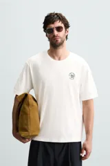 Camiseta blanca de corte holgado, cuello redondo y mangas cortas. Presenta un bordado y estampado combinado en el frente.