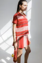 Remera polo tejida a rayas horizontales rojas y rosadas, con cuello clásico y bordado de ají verde.