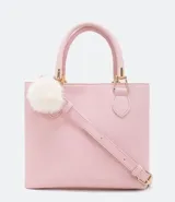 Cartera femenina cuadrada de tamaño mediano, color rosa pastel, con cierre superior y pompón blanco colgante. Incluye asa corta y correa larga extraíble.
