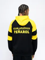 Campera deportiva negra con capucha y detalles en amarillo, cierre frontal y escudo del Club Atlético Peñarol en el pecho. Presenta cortes y cambios de color en mangas y cuerpo, y un estampado en la espalda.