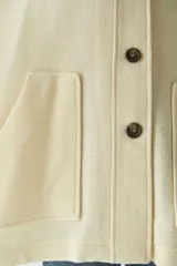 Capa con cuello, cierre frontal con botones y bolsillos delanteros. Confeccionada en lana fina sin teñir, diseñada exclusivamente por Don Baez.