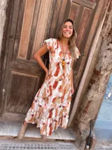 Vestido largo con estampado abstracto en tonos camel, naranja y blanco, con escote en V, mangas cortas con volados y falda con volados en el ruedo.