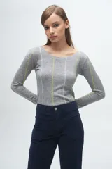 Remera gris de corte ajustado, con cuello redondo y mangas largas. Presenta líneas verticales bordadas en color verde claro y blanco.