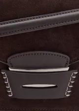 Bolso de hombro rectangular de piel de serraje color marrón oscuro, con solapa curva y cierre metálico central. Presenta costuras decorativas blancas en los laterales y una correa fina de hombro.