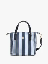 Cartera tote pequeña de lona a rayas verticales azules y blancas, con doble asa corta de mano y correa larga extraíble al hombro, ambas en cuero sintético azul marino. Tiene cierre superior con cremallera, bolsillo interno con cremallera y logo de Tommy Hilfiger en dorado en el frente.