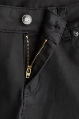 Jean de cinco bolsillos color negro, con tiro bajo y cierre de botón. Presenta un corte ajustado en la parte superior y piernas acampanadas.