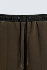 Pantalón jogger color verde oliva, corte relaxed fit, con cintura elástica ajustable con cordón, bolsillos laterales y detalle de bolsillo de vivo en la espalda. Presenta una banda lateral color crema a contraste.