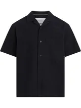 Camisa negra de manga corta con cuello cubano y bolsillo de parche en el pecho. Cierre frontal con botones y logo de la marca en el bolsillo.