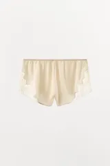 Shorts tipo lencero color crema confeccionado en tejido satinado con tiro alto, cintura elástica y detalle de encaje a tono en el ruedo.