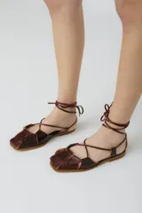 Sandalias chatitas de cuero color bordó, con puntera cuadrada y tiras finas que se atan al tobillo.