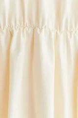 Vestido corto color crema con escote en V pronunciado, mangas globo cortas con diseño raglán, costura elástica en la cintura y pollera globo con volumen.