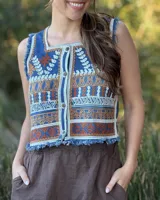 Chaleco corto de denim azul con bordado artesanal en tonos naranja, blanco y marrón. Tiene escote cuadrado, cierre de botones y terminaciones desflecadas.