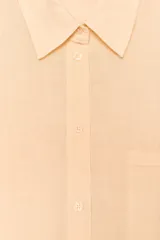 Camisa color durazno confeccionada en algodón, de corte amplio, con cuello solapa, manga larga con puños abotonados, hombros caídos, bolsillo de parche en el pecho, pinzas en la espalda y cierre frontal con botones.