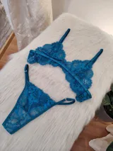 Conjunto de lencería de dos piezas (corpiño y bombacha tipo colaless/tanga) de encaje floral, color verde petróleo/turquesa oscuro. El corpiño es triangular con tirantes ajustables y la bombacha es de corte bajo con bordes festoneados.