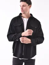 Sobrecamisa negra de corte recto con cuello clásico, cierre frontal con botones a presión, dos bolsillos de parche en el pecho y puños abotonados.