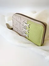 Billetera pequeña de cuero con cierre metálico, diseño color block en verde lima y beige con detalle de cordones cruzados.