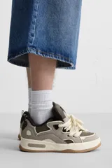 Zapatilla deportiva estilo skate color gris y verde, con cordones anchos color crema, lengüeta acolchada, tirador trasero y suela gruesa de goma color caramelo.