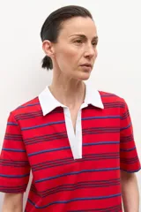 Remera de manga corta con cuello polo blanco y escote pronunciado en V. El cuerpo de la prenda es de color rojo con finas rayas horizontales en azul oscuro y azul claro.