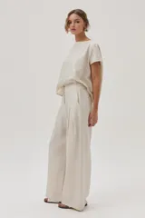 Pantalón de lino color beige, de pierna ancha, con botón en la cintura, pinzas en el frente y bolsillos delanteros y traseros.