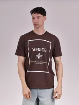 Remera marrón de manga corta con estampa frontal que incluye la palabra 'Venice', un oso con una tabla de surf y la frase 'Venice Beach, California - Locals Only'.