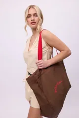 Bolso tote de lona color beige claro con asas negras. Presenta un estampado de texto curvo en negro en el frente que dice "BeGanesha".