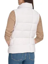 Chaleco blanco acolchado con cuello alto y cierre frontal con cremallera dorada. Tiene bolsillos laterales con cremallera y logo de la marca en el tirador.