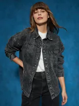 Sobrecamisa negra de denim con cuello clásico, cierre frontal con botones a presión, mangas largas con puños abotonados, dos bolsillos con solapa en el pecho y corte holgado.