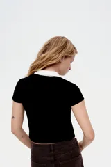 Camisa negra de punto acanalado con cuello blanco, manga corta y botonadura frontal.