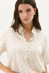 Camisa blanca con estampado de lunares negros, de corte clásico, manga corta y cuello camisero.