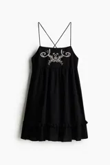 Vestido corto negro de algodón con breteles finos cruzados en la espalda, escote cuadrado, bordado floral en el busto y volados en el ruedo.