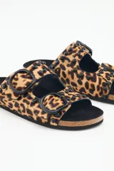 Sandalia tipo birkenstock de pelo con estampado animal print (leopardo), con dos tiras ajustables con hebillas negras y tachas metálicas negras. La plantilla es de corcho y la suela de goma eva.