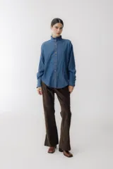 Camisa celeste de jean con cuello alto con volados y mangas largas abullonadas con puños con volados. Presenta botones de madera y costuras rojas a contraste.